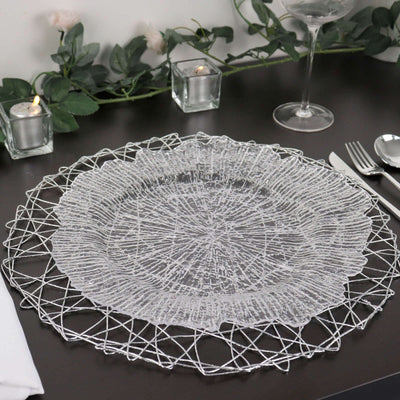 Decorative silver table placemat on a dark table with candles and greenery.