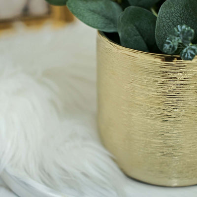 Gold textured planter with greenery on a soft white surface.