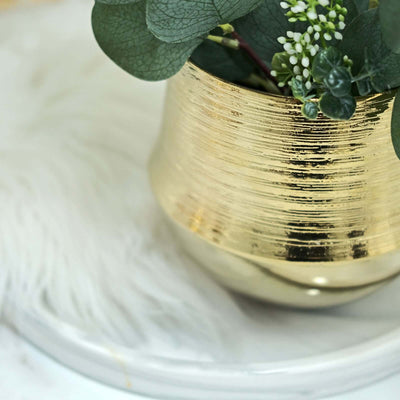 Gold textured planter with greenery on a marble tray.