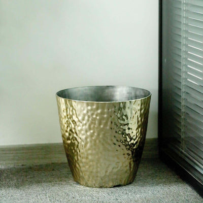 Hammered gold metal planter on a textured surface.