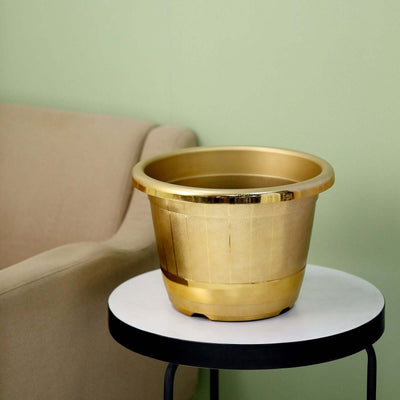 Gold decorative planter on a white side table with a beige sofa in the background.