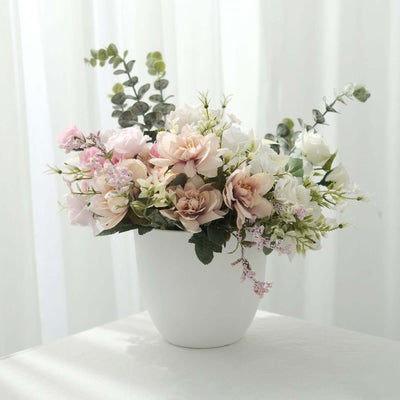 Artificial flower arrangement in a white pot against a bright backdrop.