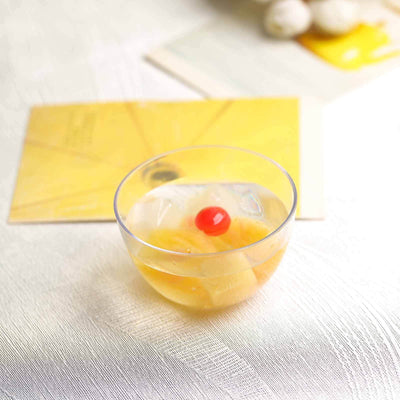 Glass bowl of fruit cocktail with cherry on top, on textured surface.