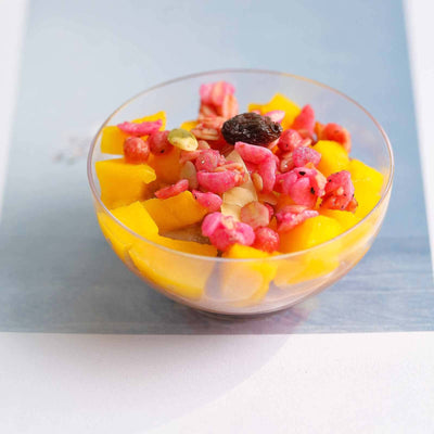 Colorful fruit salad with mango, pink berries, and nuts in a clear bowl.