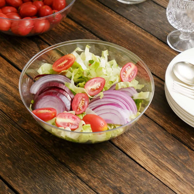 Fresh salad with lettuce, tomatoes, and red onions in a clear bowl on a wooden table.