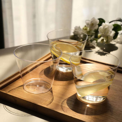 Three clear glasses with lemon slices on a wooden tray in natural light.