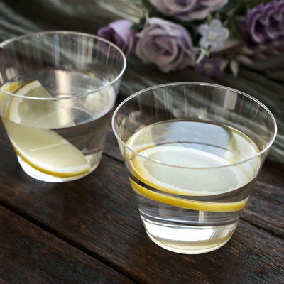 Two clear cups of water with lemon slices on a wooden table.