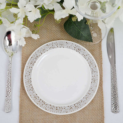 Elegant white plate with intricate silver trim, surrounded by floral decor and cutlery.