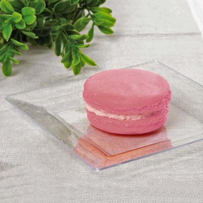 Pink macaron on a glass plate with greenery in the background.