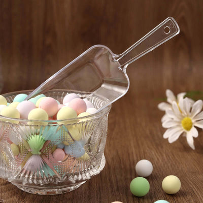 Clear scoop with pastel candy in decorative bowl on wooden surface.