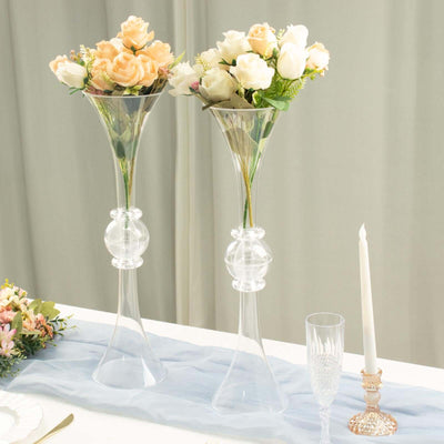 Elegant clear glass flower vases with artificial roses and candles on a table.