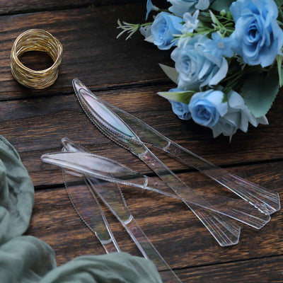 Clear plastic knives with blue flowers and a gold ring on a wooden surface.