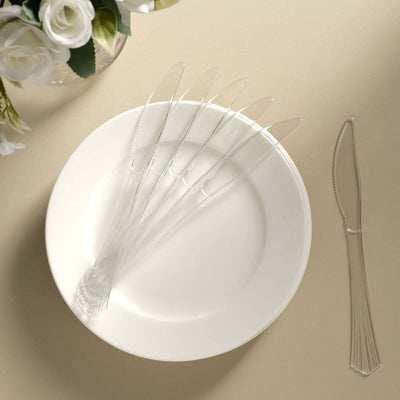 Clear plastic knives arranged on a white plate against a neutral background.