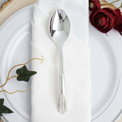 Silver spoon on a white napkin with decorative flowers and greenery.