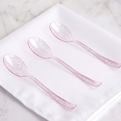 Set of three sparkling pink spoons on a white napkin.