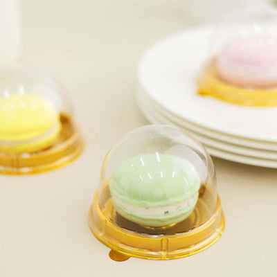Colorful macarons in clear domes on a table with plates in the background.