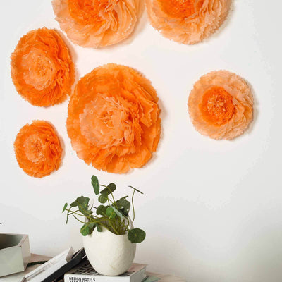 Orange paper flowers mounted on a wall with a potted plant in a white vase.