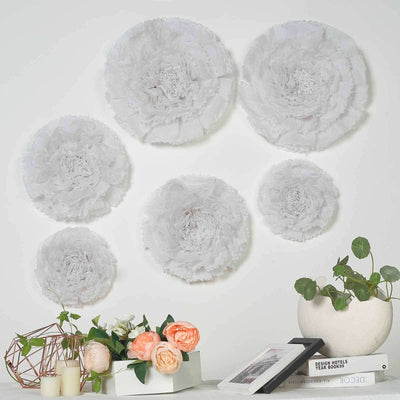 Decorative white paper flowers on a wall with plants and decor items in the foreground.