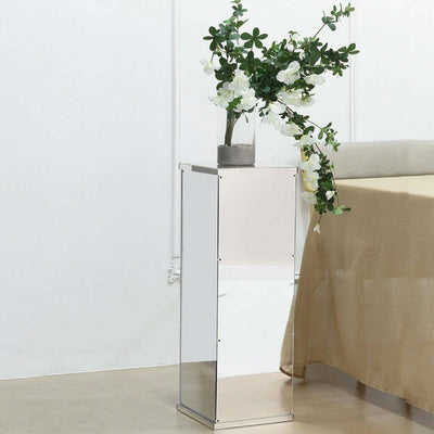 Mirrored side table with a vase of flowers on top against a plain backdrop.