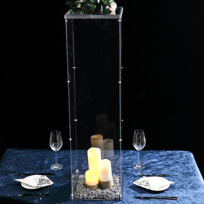 Tall acrylic candle holder with decorative stones and candles, set on an elegant table.