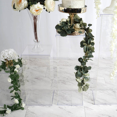 Acrylic display stands with floral arrangements and a cake on a marble background.