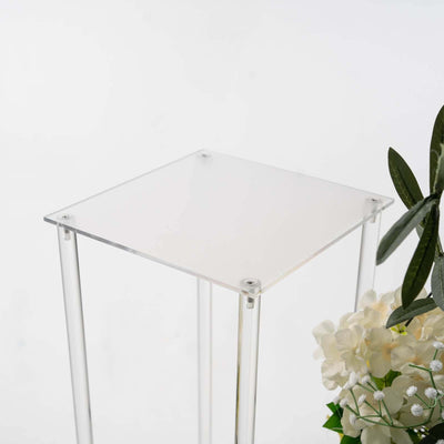 Acrylic plant stand with clear legs and square top against a white background