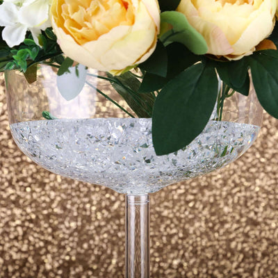 Crystal vase with flowers and decorative stones against a glittery gold background.