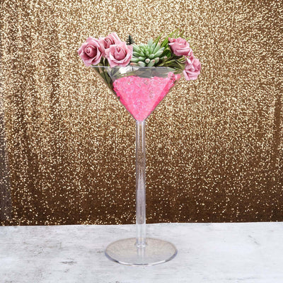 Decorative martini glass with pink flowers and rocks on a glittery gold background.