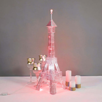 Eiffel Tower lamp with pink light and decorative candles on a table.