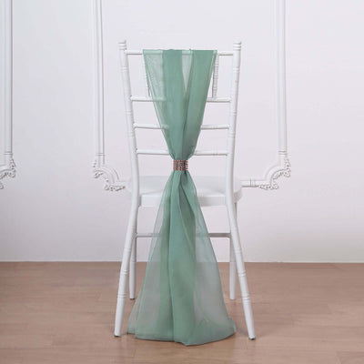 Green chiffon chair sash tied on a white chair in a minimalist setting.