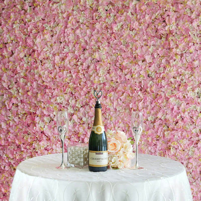 Champagne bottle with flutes and flowers on a table against a pink petal backdrop.