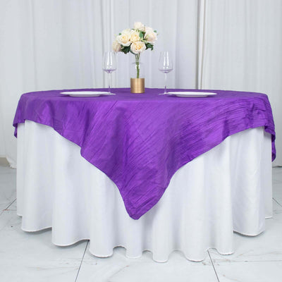 Purple tablecloth draped elegantly over a round white table with floral centerpiece.