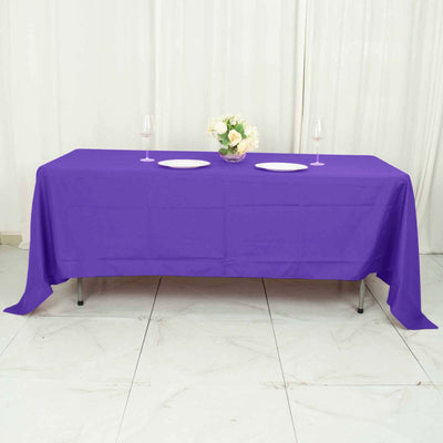 Purple tablecloth draped over a table set with plates and a floral centerpiece.