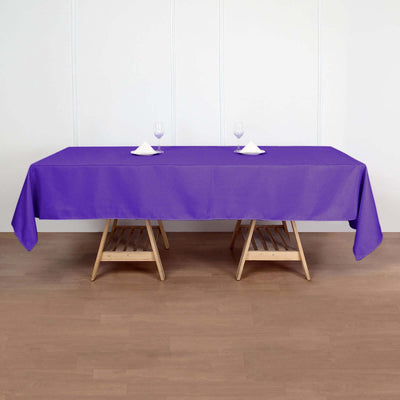 Purple tablecloth on wooden tables set for dining with wine glasses.
