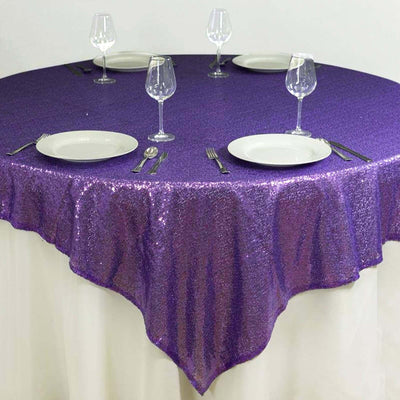Purple sequin tablecloth draped over a round table with plates and glasses.