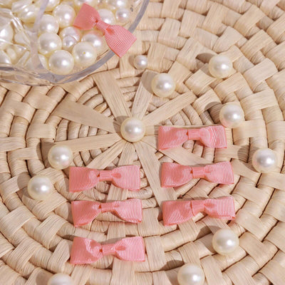 Pink ribbon bows arranged with pearls on a woven surface.