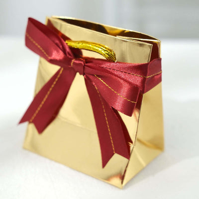 Gold gift bag with red ribbon bow on a white background.