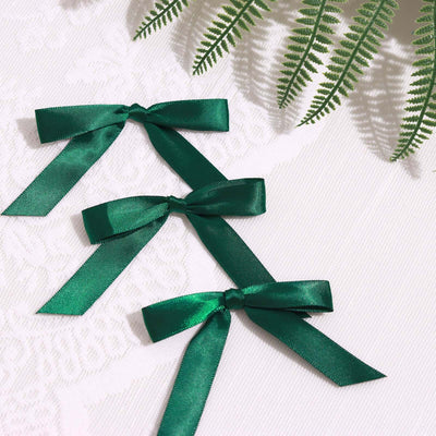 Green satin ribbon bows arranged on a textured white surface.