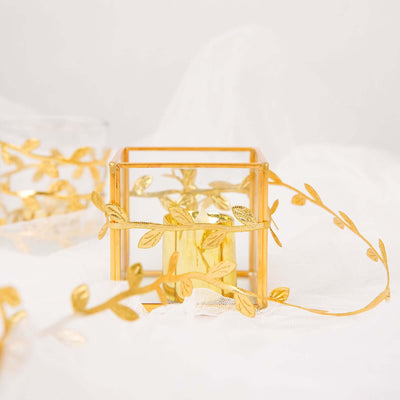Glass candle holder with golden leaf accents on a soft background.