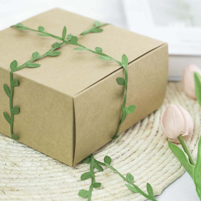 Gift box wrapped with green vine decoration on a woven mat.