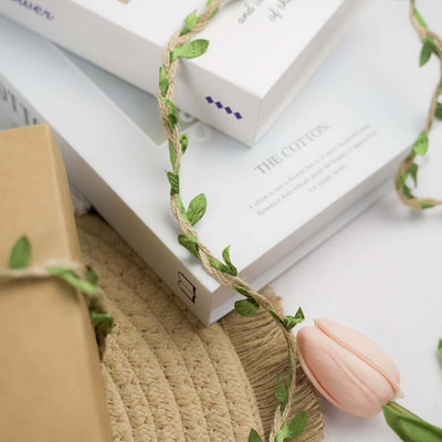 Decorative floral twine with a pink flower on stacked books and a straw hat.