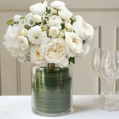 White floral arrangement in a glass vase with green accents.