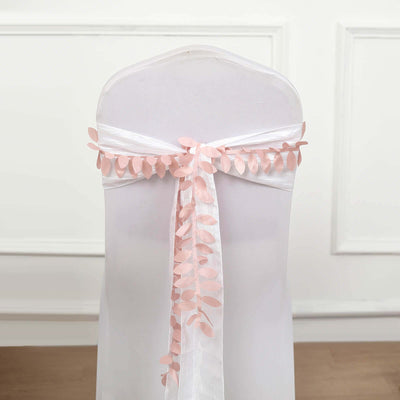 Pink leaf chair sash tied on a white chair against a plain backdrop.