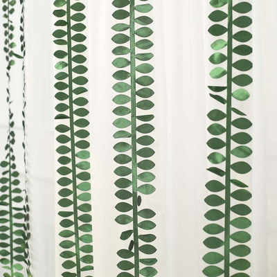 Green leaf-patterned sheer curtain hanging in a room.