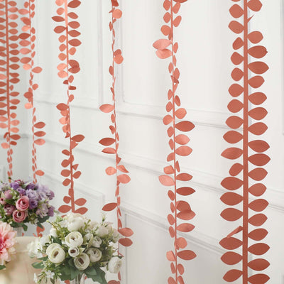 Decorative paper leaf garlands hanging on a wall with floral arrangements below.