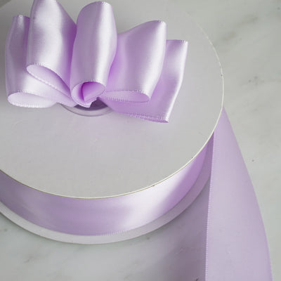 Purple satin ribbon roll with a bow on a white background.