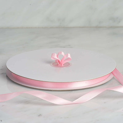 Pink satin ribbon on a spool with a decorative bow.
