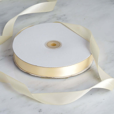 Gold satin ribbon spool with loose ribbon on a marble surface.
