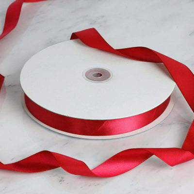 Red satin ribbon on a spool with loose ribbon curled around it.