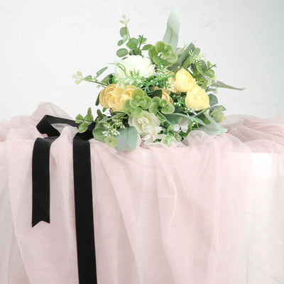 Floral arrangement with yellow roses and greenery on a soft pink fabric backdrop.